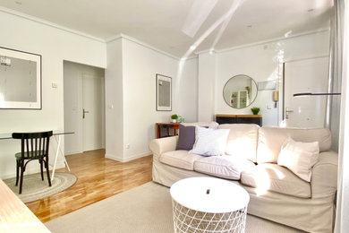 Modelo de salón abierto y beige y blanco de tamaño medio con paredes blancas, suelo de madera en tonos medios, televisor independiente y suelo marrón