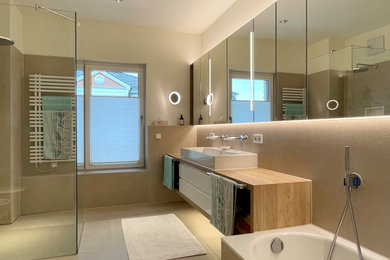 Großes Modernes Badezimmer mit flächenbündigen Schrankfronten, weißen Schränken, Einbaubadewanne, bodengleicher Dusche, Wandtoilette, beigen Fliesen, Keramikfliesen, weißer Wandfarbe, Keramikboden, Aufsatzwaschbecken, beigem Boden, offener Dusche und Doppelwaschbecken in Köln