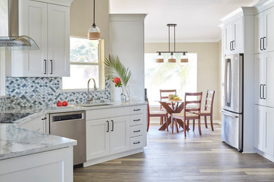 Inspiration for a mid-sized coastal vinyl floor, multicolored floor and vaulted ceiling open concept kitchen remodel in Other with an undermount sink, recessed-panel cabinets, white cabinets, quartz countertops, blue backsplash, ceramic backsplash, stainless steel appliances and multicolored countertops