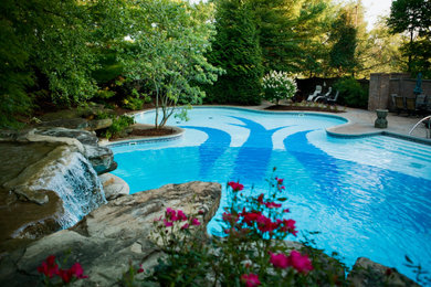 Huge transitional backyard stamped concrete and custom-shaped pool landscaping photo in Other