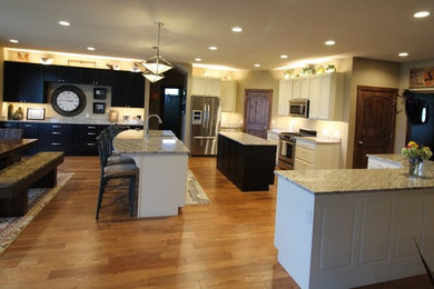 Example of a huge classic medium tone wood floor open concept kitchen design in Other with a farmhouse sink, recessed-panel cabinets, white cabinets, granite countertops, stainless steel appliances and two islands