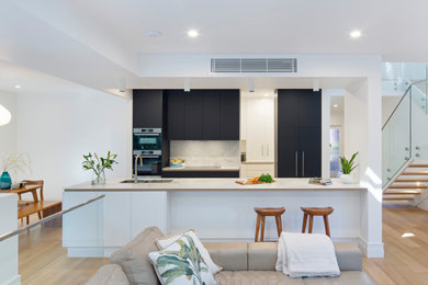 This is an example of a large contemporary galley open plan kitchen in Sydney with an undermount sink, flat-panel cabinets, black cabinets, marble benchtops, white splashback, stone slab splashback, stainless steel appliances, medium hardwood floors, with island, brown floor and white benchtop.
