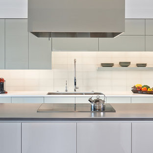 Modelo de cocina comedor en U, contemporánea, grande, con armarios con paneles lisos, suelo de madera oscura, una isla, fregadero de doble seno, puertas de armario blancas, encimera de cuarzo compacto, electrodomésticos con paneles, salpicadero blanco, salpicadero de azulejos de vidrio y suelo marrón