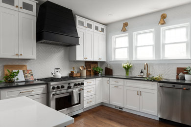 Example of a mid-sized trendy medium tone wood floor and brown floor eat-in kitchen design in Chicago with an undermount sink, shaker cabinets, black cabinets, quartz countertops, white backsplash, porcelain backsplash, stainless steel appliances and an island