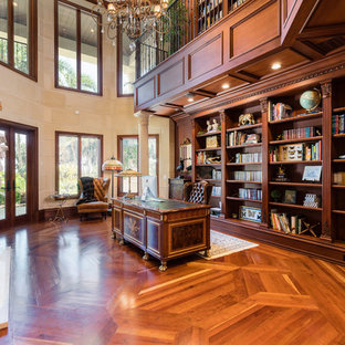 Esempio di un ampio studio mediterraneo con libreria, pareti beige, pavimento in legno massello medio, camino classico, cornice del camino in pietra, scrivania autoportante e pavimento marrone