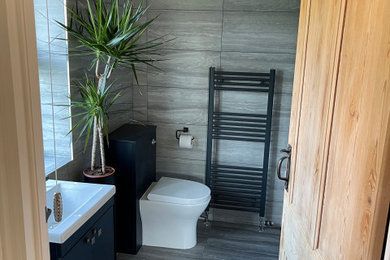 Design ideas for a medium sized contemporary family bathroom in Essex with flat-panel cabinets, black cabinets, an alcove bath, a shower/bath combination, grey tiles, ceramic tiles, ceramic flooring, grey floors, feature lighting, a single sink and a built in vanity unit.