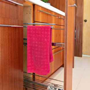 サンディエゴの小さいモダンスタイルのおしゃれな家事室 (アンダーカウンターシンク、フラットパネル扉のキャビネット、中間色木目調キャビネット、クオーツストーンカウンター、赤い壁、淡色無垢フローリング、目隠し付き洗濯機・乾燥機、茶色い床、白いキッチンカウンター) の写真