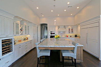 Transitional dark wood floor kitchen photo in Phoenix with a farmhouse sink, raised-panel cabinets, white cabinets, granite countertops, multicolored backsplash, glass tile backsplash, paneled appliances and an island
