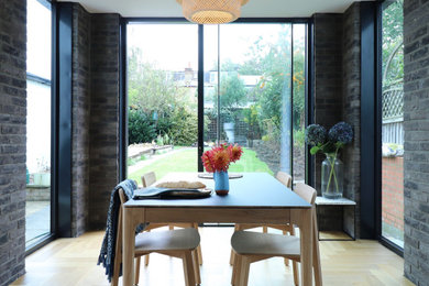 This is an example of a medium sized contemporary dining room in London with brick walls, grey walls, light hardwood flooring and beige floors.