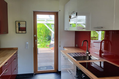 Geschlossene, Zweizeilige, Mittelgroße Moderne Küche ohne Insel mit integriertem Waschbecken, flächenbündigen Schrankfronten, weißen Schränken, Arbeitsplatte aus Holz, Küchenrückwand in Rot, Glasrückwand, schwarzen Elektrogeräten, Porzellan-Bodenfliesen, schwarzem Boden und Tapete in Frankfurt am Main