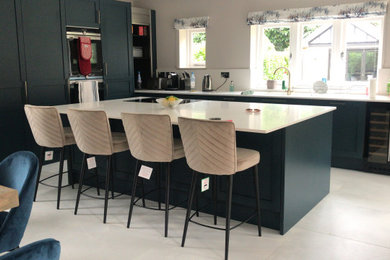 This is an example of a large contemporary l-shaped kitchen/diner in Dorset with a submerged sink, shaker cabinets, blue cabinets, granite worktops, white splashback, granite splashback, black appliances, marble flooring, an island, white floors and white worktops.