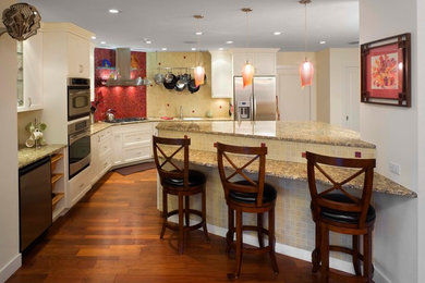 Open concept kitchen - mid-sized eclectic l-shaped medium tone wood floor open concept kitchen idea in Tampa with a double-bowl sink, shaker cabinets, white cabinets, granite countertops, beige backsplash, glass tile backsplash, stainless steel appliances and an island