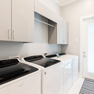 This is an example of a large modern single-wall separated utility room in Orlando with flat-panel cabinets, grey cabinets, grey walls, porcelain flooring, a side by side washer and dryer and white floors.