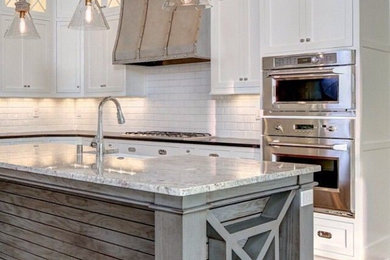 Inspiration for a mid-sized transitional l-shaped medium tone wood floor kitchen remodel in San Diego with a farmhouse sink, recessed-panel cabinets, white cabinets, granite countertops, white backsplash, subway tile backsplash, stainless steel appliances and an island