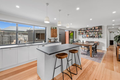 Inspiration for a mid-sized modern galley eat-in kitchen in Melbourne with an undermount sink, recessed-panel cabinets, white cabinets, laminate benchtops, white splashback, ceramic splashback, white appliances, medium hardwood floors, with island and black benchtop.