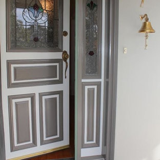 Cette photo montre une porte d'entrée éclectique avec un mur gris, un sol en bois brun, une porte simple et une porte grise.