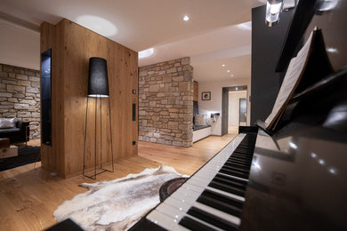 Mittelgroßes, Offenes Industrial Musikzimmer mit weißer Wandfarbe, braunem Holzboden, Eckkamin, verputzter Kaminumrandung, Multimediawand und braunem Boden in Sonstige