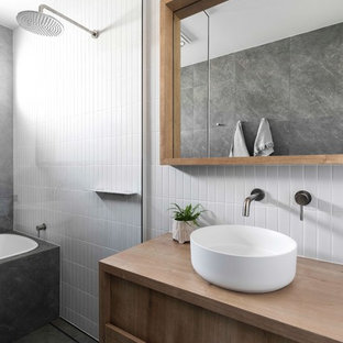 This is an example of a contemporary wet room bathroom in Brisbane with a drop-in tub, a vessel sink, wood benchtops, an open shower, recessed-panel cabinets, medium wood cabinets, white tile, grey floor and brown benchtops.