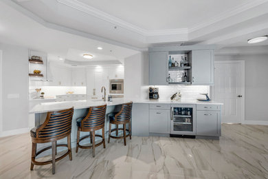 Large trendy single-wall ceramic tile, multicolored floor and tray ceiling open concept kitchen photo in Miami with an undermount sink, shaker cabinets, white cabinets, quartz countertops, white backsplash, subway tile backsplash, stainless steel appliances, a peninsula and white countertops