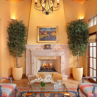 Foto de salón mediterráneo con paredes amarillas, chimenea tradicional y marco de chimenea de piedra