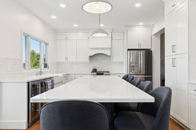 Eat-in kitchen - mid-sized transitional medium tone wood floor and brown floor eat-in kitchen idea in Philadelphia with a farmhouse sink, shaker cabinets, white cabinets, quartz countertops, white backsplash, porcelain backsplash, stainless steel appliances, an island and white countertops