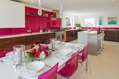 This is an example of an expansive modern u-shaped kitchen in London with an undermount sink, flat-panel cabinets, solid surface benchtops, pink splashback, glass sheet splashback, stainless steel appliances and with island.
