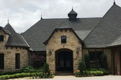 Large traditional beige two-story stone house exterior idea in Other with a clipped gable roof and a shingle roof