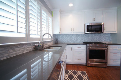 Example of a mid-sized transitional l-shaped medium tone wood floor and brown floor open concept kitchen design in Atlanta with a double-bowl sink, shaker cabinets, white cabinets, quartz countertops, gray backsplash, matchstick tile backsplash, stainless steel appliances, an island and white countertops