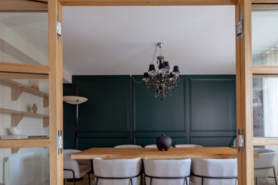 Cette image montre une grande salle à manger design avec un mur vert, parquet clair, boiseries et verrière.