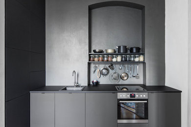 Einzeilige, Mittelgroße, Offene Moderne Küche ohne Insel mit Einbauwaschbecken, flächenbündigen Schrankfronten, schwarzen Schränken, Mineralwerkstoff-Arbeitsplatte, Rückwand aus Stein, braunem Boden, Küchenrückwand in Schwarz, braunem Holzboden, schwarzer Arbeitsplatte und Küchengeräten aus Edelstahl in Berlin