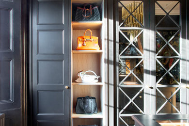 Large classic gender neutral dressing room in Edinburgh with glass-front cabinets, black cabinets, light hardwood flooring and beige floors.