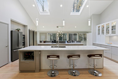 This is an example of a large modern galley eat-in kitchen in Atlanta with a single-bowl sink, flat-panel cabinets, white cabinets, quartz benchtops, grey splashback, ceramic splashback, stainless steel appliances, light hardwood floors, multiple islands, brown floor and white benchtop.