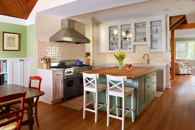 Eat-in kitchen - mid-sized cottage l-shaped medium tone wood floor eat-in kitchen idea in Philadelphia with an undermount sink, glass-front cabinets, white cabinets, wood countertops, beige backsplash, stainless steel appliances, an island and ceramic backsplash