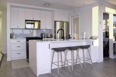 Inspiration for a mid-sized contemporary galley porcelain tile and beige floor enclosed kitchen remodel in Vancouver with an undermount sink, shaker cabinets, white cabinets, solid surface countertops, gray backsplash, glass sheet backsplash, stainless steel appliances, a peninsula and white countertops