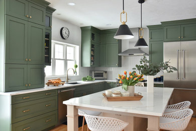 На фото: кухня в стиле неоклассика (современная классика) с зелеными фасадами, столешницей из кварцевого агломерата, техникой из нержавеющей стали, островом и белой столешницей