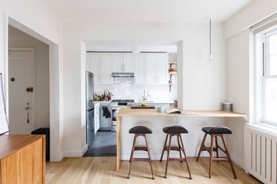 Example of a small minimalist l-shaped porcelain tile and gray floor eat-in kitchen design in New York with an undermount sink, shaker cabinets, white cabinets, quartz countertops, white backsplash, subway tile backsplash, stainless steel appliances, a peninsula and white countertops