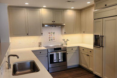 高級な中くらいなトランジショナルスタイルのおしゃれなコの字型キッチン (アンダーカウンターシンク、フラットパネル扉のキャビネット、ベージュのキャビネット、クオーツストーンカウンター、白いキッチンパネル、モザイクタイルのキッチンパネル、パネルと同色の調理設備、クッションフロア、アイランドなし、茶色い床、白いキッチンカウンター) の写真
