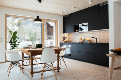 Offene Moderne Küche in L-Form mit Waschbecken, schwarzen Schränken, Küchenrückwand in Weiß, grauem Boden und schwarzer Arbeitsplatte in München