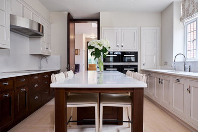 Design ideas for a large classic u-shaped enclosed kitchen in London with a submerged sink, recessed-panel cabinets, beige cabinets, white splashback, black appliances, an island, beige floors, white worktops and limestone flooring.