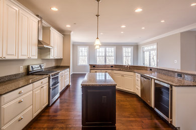 Photo of a large traditional u-shaped open plan kitchen in Baltimore with an undermount sink, raised-panel cabinets, white cabinets, granite benchtops, brown splashback, stone slab splashback, stainless steel appliances, medium hardwood floors, multiple islands and brown floor.