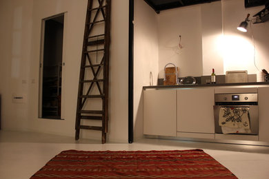 Foto di una piccola cucina ad ambiente unico moderna con lavello da incasso, ante bianche, top in laminato, paraspruzzi grigio, elettrodomestici in acciaio inossidabile, pavimento in cemento e nessuna isola