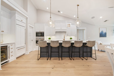 Inspiration for a large coastal l-shaped light wood floor, brown floor and vaulted ceiling eat-in kitchen remodel in Other with a drop-in sink, shaker cabinets, white cabinets, quartz countertops, white backsplash, ceramic backsplash, stainless steel appliances, an island and white countertops