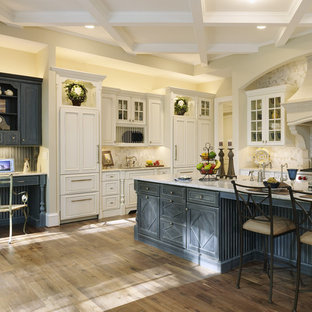 Modelo de cocina en L, tradicional, extra grande, con fregadero sobremueble, armarios con rebordes decorativos, puertas de armario blancas, encimera de granito, salpicadero beige, salpicadero de losas de piedra, electrodomésticos de acero inoxidable, suelo de madera oscura, una isla y suelo marrón