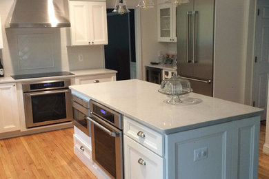 Open concept kitchen - mid-sized transitional l-shaped medium tone wood floor and brown floor open concept kitchen idea in DC Metro with a farmhouse sink, shaker cabinets, white cabinets, quartz countertops, white backsplash, subway tile backsplash, stainless steel appliances and an island
