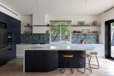 This is an example of a large contemporary galley open plan kitchen in Melbourne with a double-bowl sink, beaded cabinets, blue cabinets, marble worktops, blue splashback, porcelain splashback, stainless steel appliances, light hardwood flooring, an island, beige floors and white worktops.