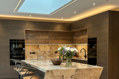 Example of a large trendy l-shaped porcelain tile and beige floor eat-in kitchen design in Other with a drop-in sink, flat-panel cabinets, dark wood cabinets, quartz countertops, beige backsplash, black appliances, an island and beige countertops