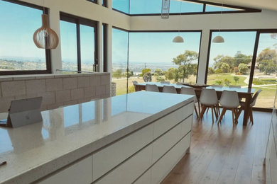This is an example of a mid-sized contemporary galley kitchen in Geelong with white cabinets, quartz benchtops and with island.