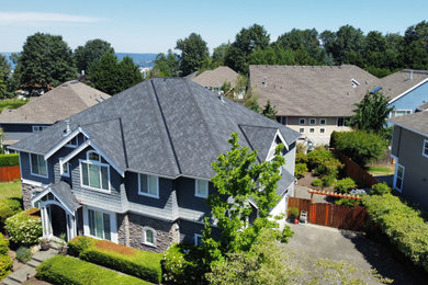 Example of a large arts and crafts blue two-story stone and shingle house exterior design in Seattle with a hip roof, a shingle roof and a black roof