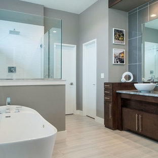 Immagine di una grande stanza da bagno padronale moderna con ante lisce, ante in legno bruno, vasca freestanding, doccia ad angolo, WC a due pezzi, piastrelle blu, piastrelle grigie, piastrelle di vetro, pareti grigie, pavimento in laminato, lavabo a bacinella, top in granito, pavimento beige e porta doccia a battente