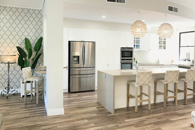 Design ideas for a mid-sized tropical u-shaped open plan kitchen in Gold Coast - Tweed with an undermount sink, shaker cabinets, white cabinets, marble benchtops, white splashback, porcelain splashback, stainless steel appliances, vinyl floors, with island, brown floor and beige benchtop.